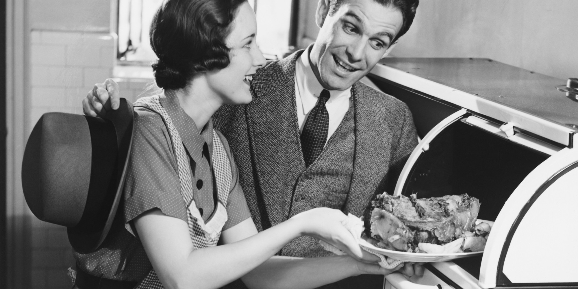 A man admiring a roast that a woman is retrieving from the oven